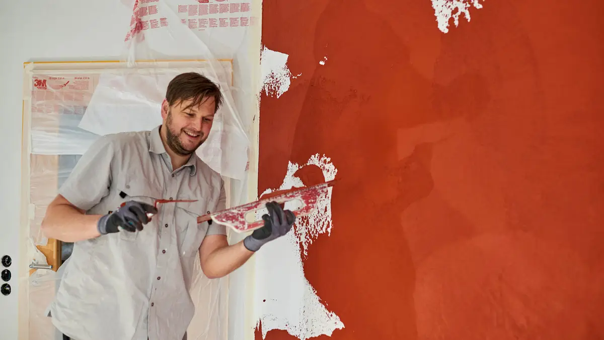 Martin Bräuninger trägt Kalkputz auf eine rote Wand auf
